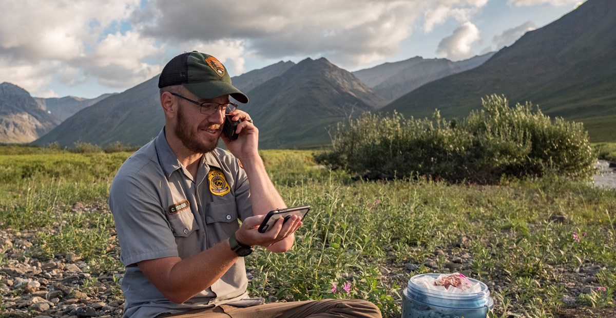 A park ranger talks on a satellite phone in a mountain valley
