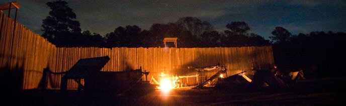 Stockade wall illuminated by fire in prison camp site.