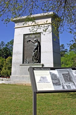 A tal granite monument rises in the distance, with an exhibit panel in the foreground.