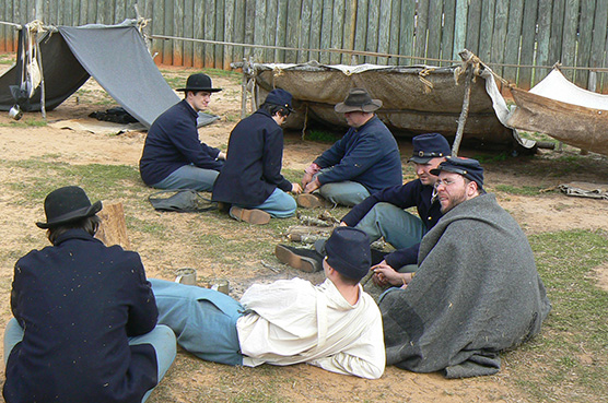Volunteers dressed as U.S. soldiers sit around a campfire.