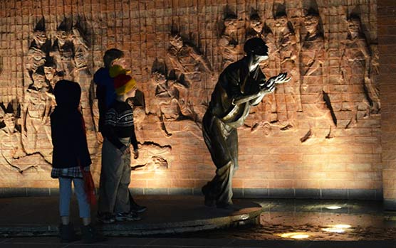 Children stand next to an illuminated sculpture at night.