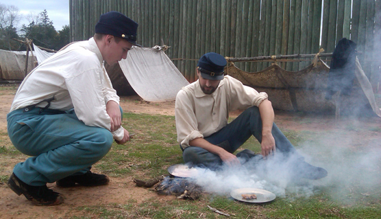 Men dressed as Union soldiers hover over a smoking campfire