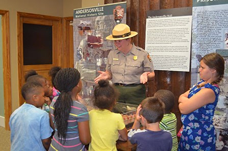 A uniformed park ranger speaks with children
