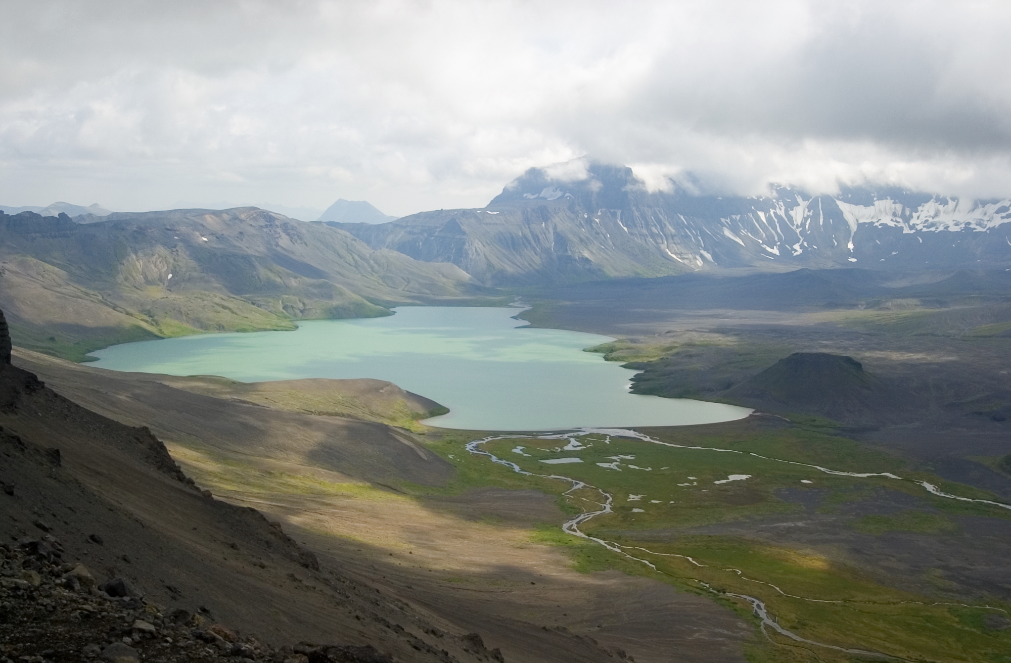 Aerial view of a lake recessed in a caldera with mountain range in the background