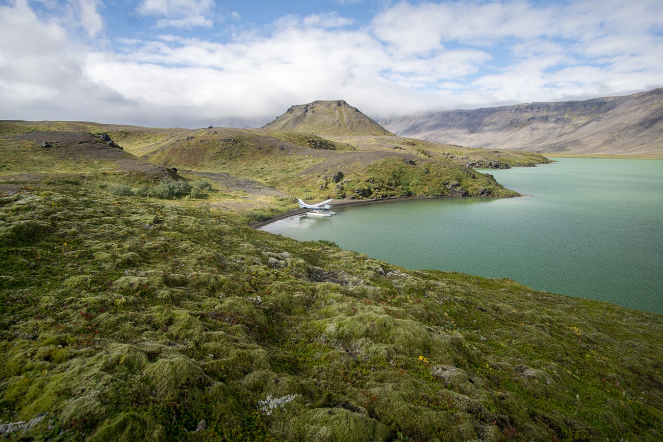tundra hummocks over a rolling volcanic landscape as a float plan sits on a lake in the middle distance