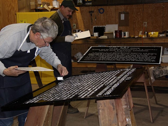 volunteer and nps staff painting iron tablet