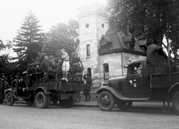 Black and white photo of soldiers on an army troop transport truck in front of a stone building.