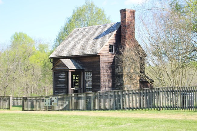 Wooden 1 1/2 story house with porch across the front of the house. There is an unpainted wooden that surrounds the house.