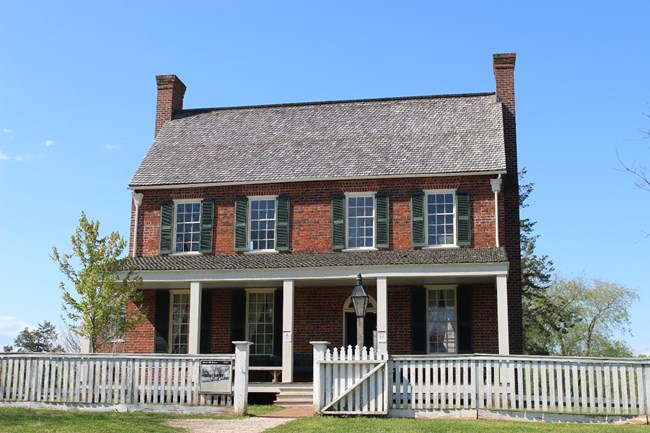 Two story brick tavern with a white picket fence in front.