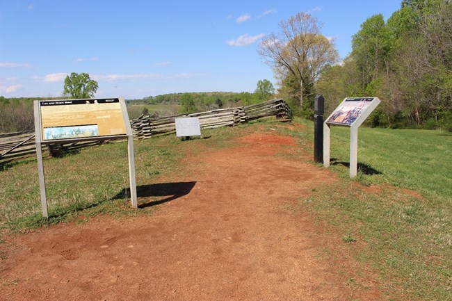 Three signs describing the location of Grant and Lee's meeting on the top of a hill with trees in the background.