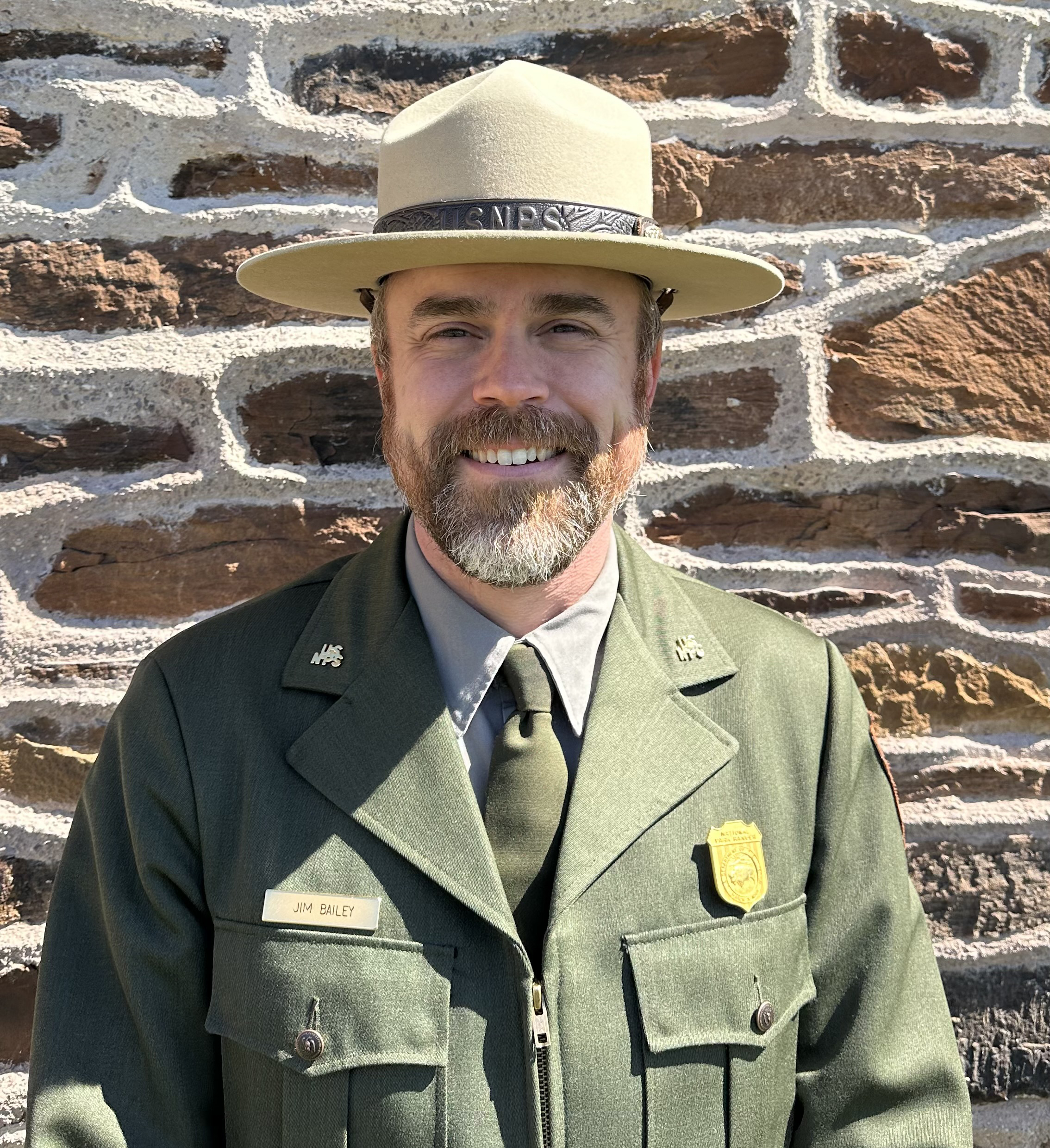 A bearded man in a green uniform smiles