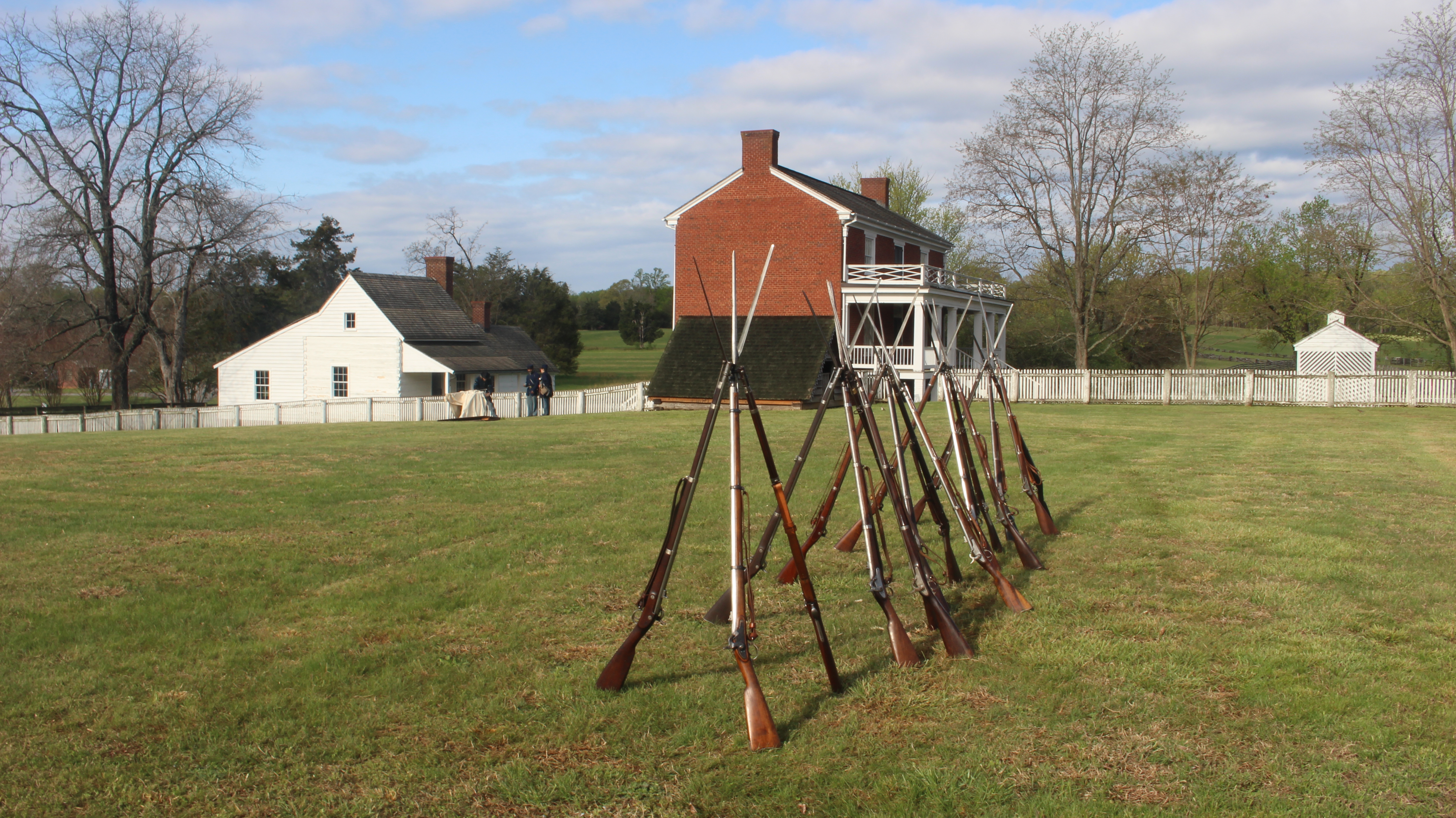 A series of stacked rifles. The McLean House is in the background