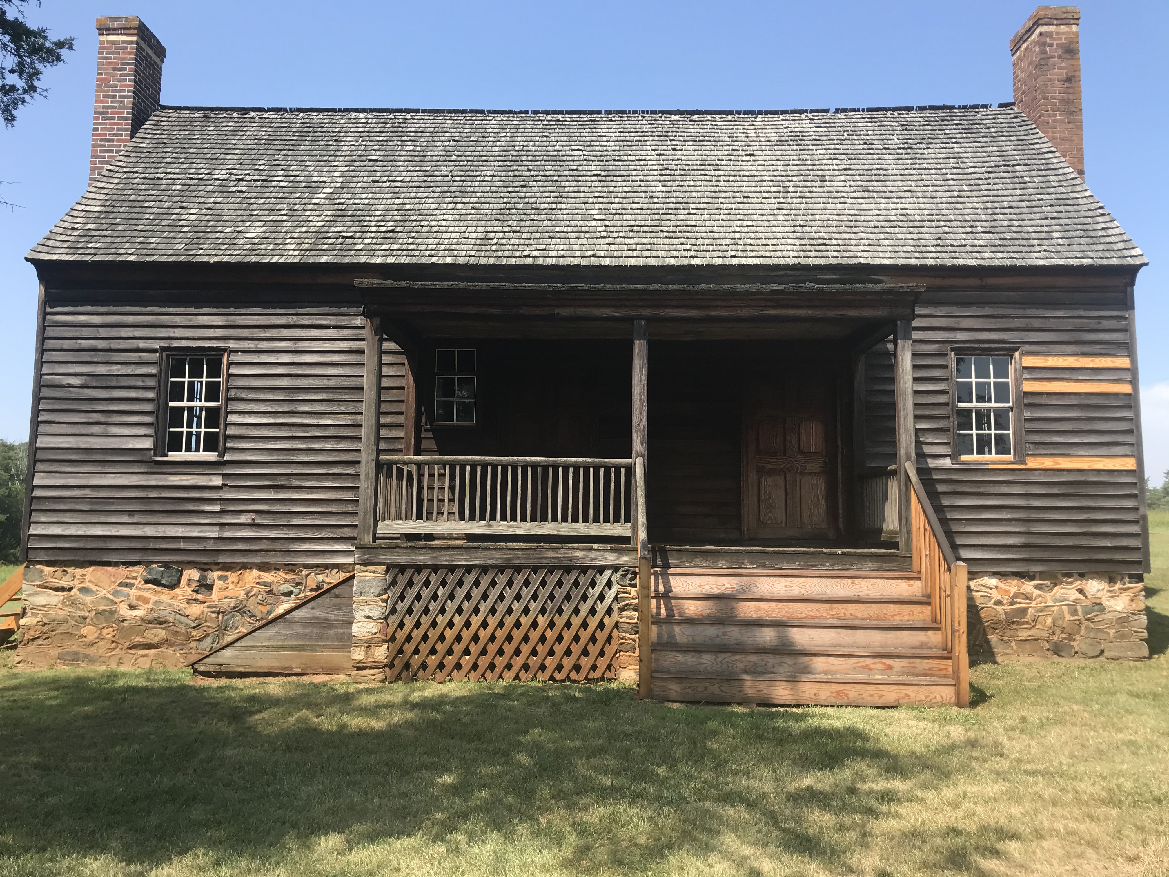 Two-story, wood-paneled home with large porch and steps, plus stone foundation. Lighter-toned panels show preservation work in the wood paneling and porch.