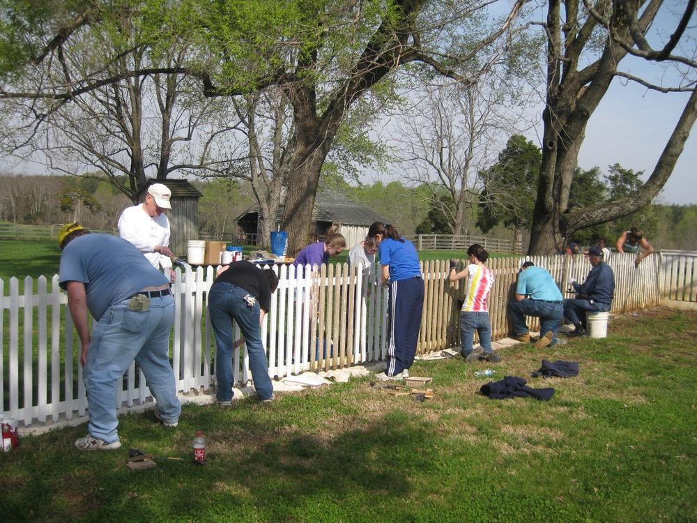 A group of volunteers paints a picket fence