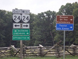 Two sign posts with directional signs for highway 24 to Richmond, Lynchburg, and Appomattox, Museum of the Confederacy, and a Tourist Info Center. In the background is a rustic wood fence and trees.