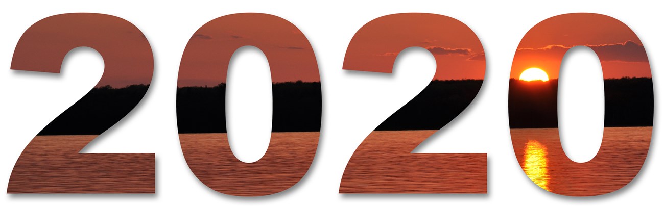 An image of sunset over a wooded island, reflected in the water, within the number 2020.