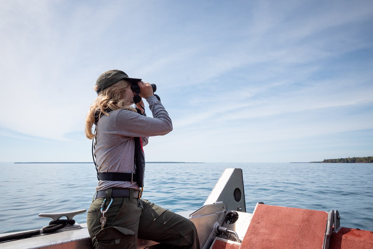 Photograph of a woman looking through binocurlars on a boat.
