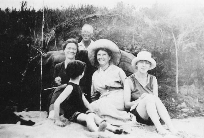 A black and white photo of four people posing for a picture sitting on the ground and smiling.