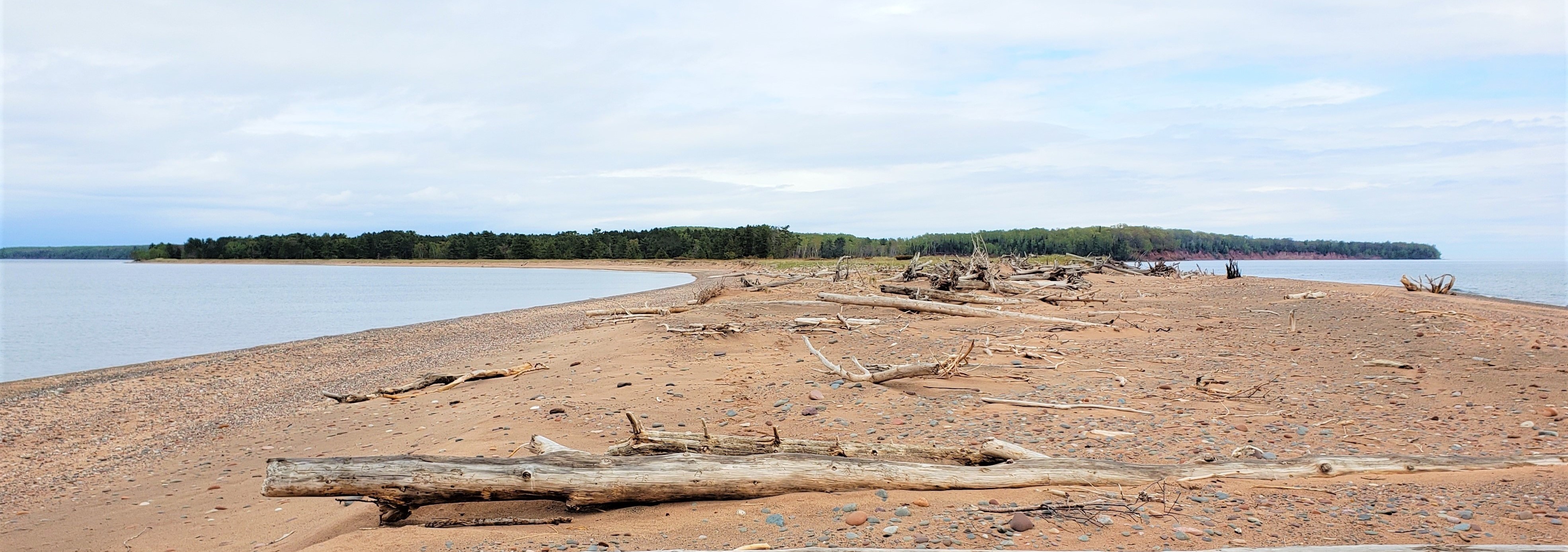 Sand and stones extending forward from a distant forest covered island.