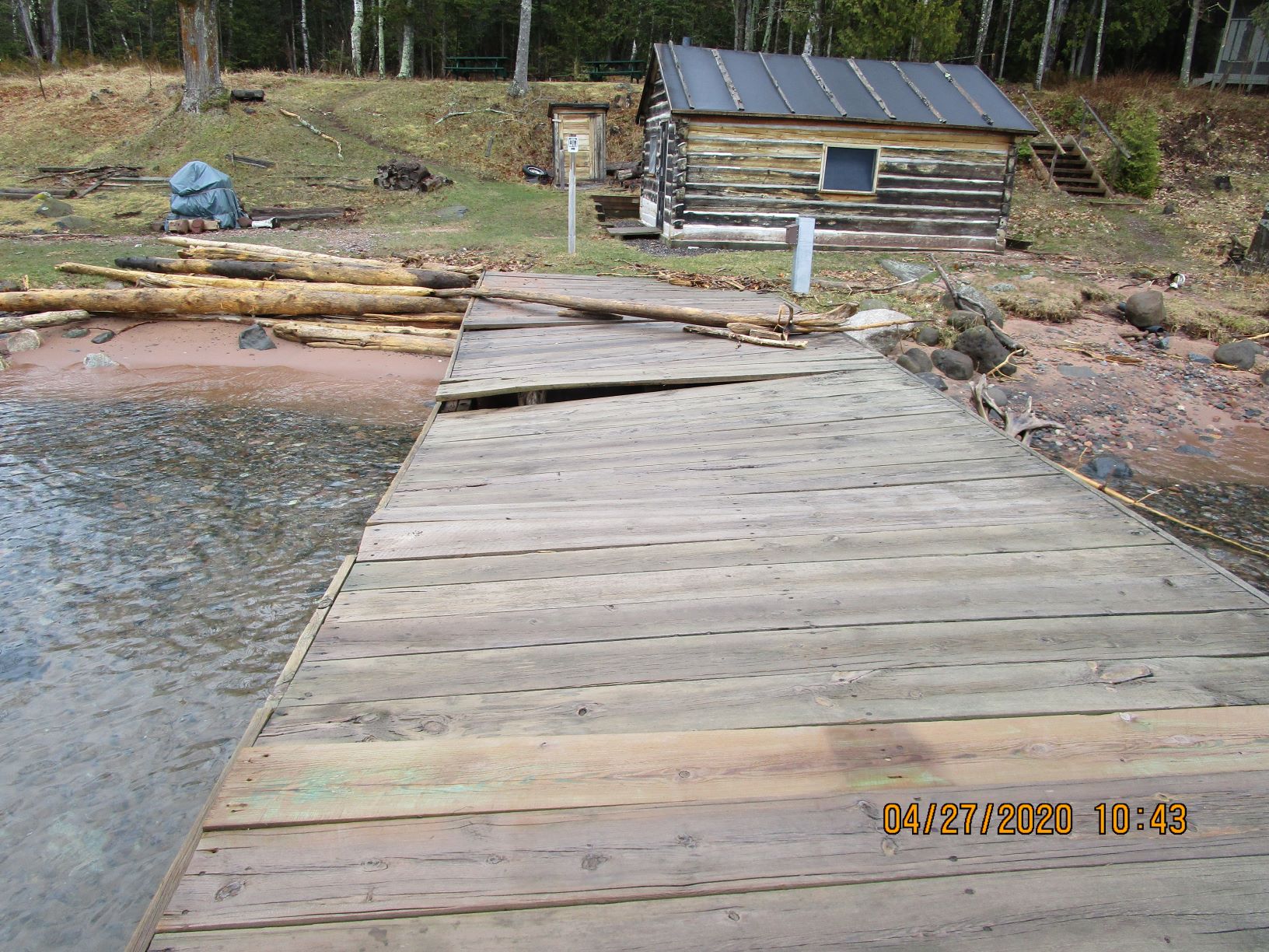 A wooden dock is twisted at an angle with boards pulled up and debris.