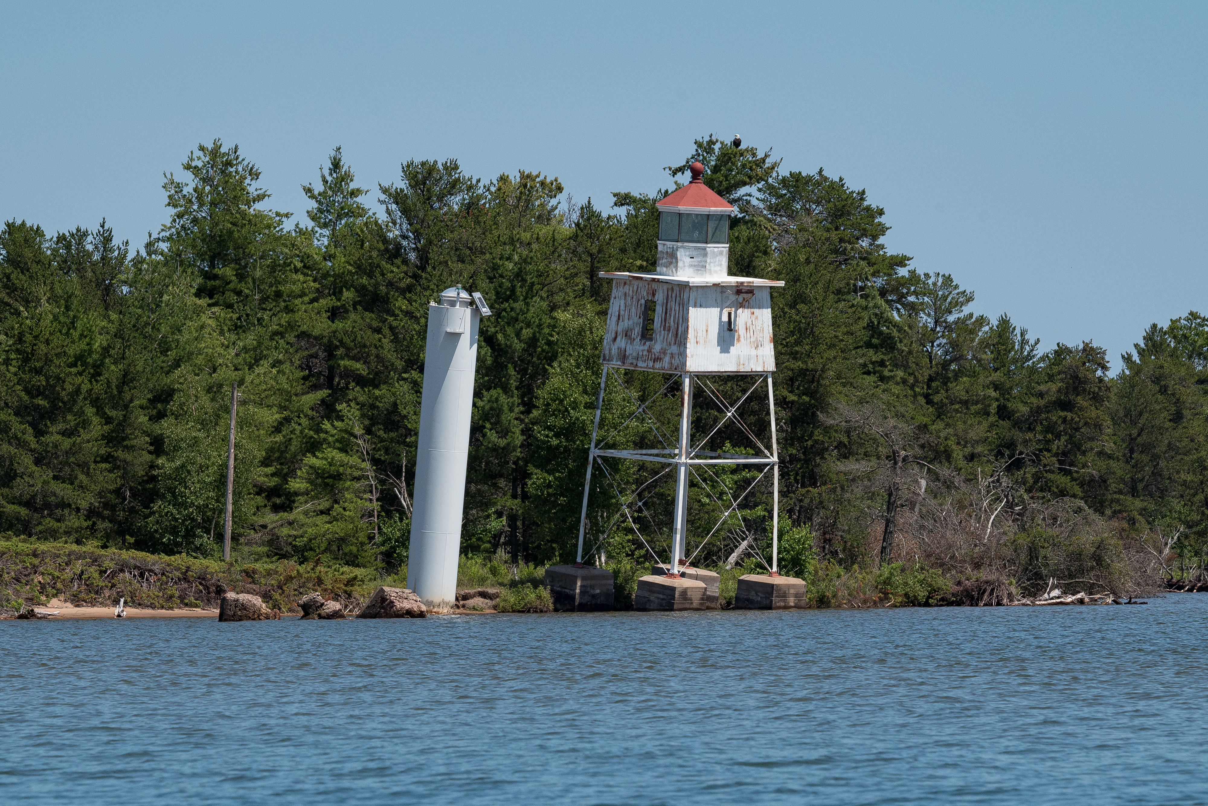 Photograph of historic steel frame light tower leaning slightly towards lake.