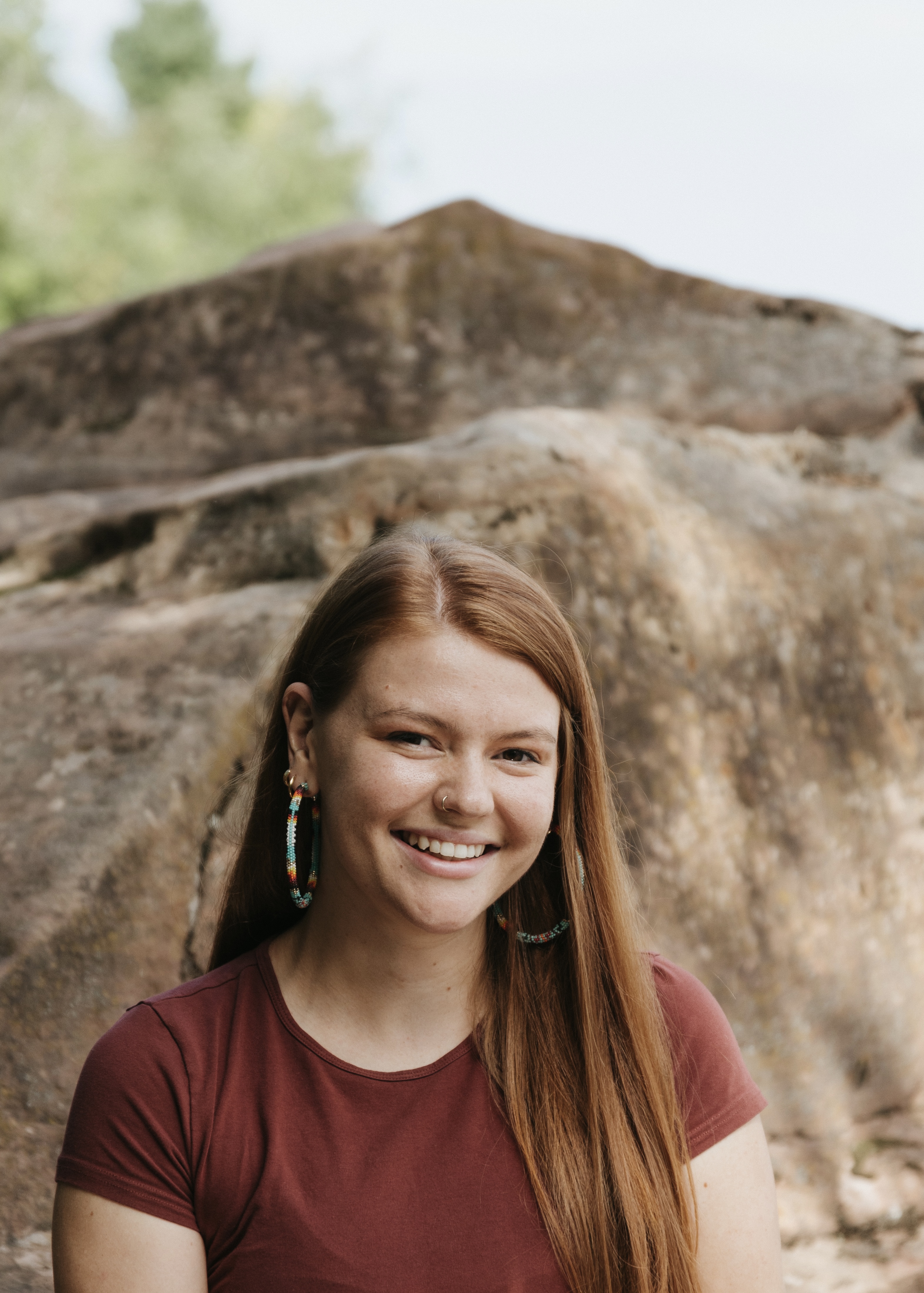 A portrait of a woman sitting in front of a large brownish red stone.