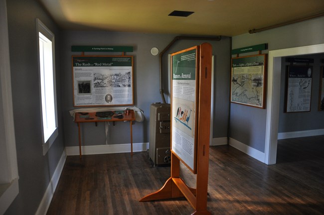 In the middle of a small room, an upright stand with an exhibit panel and two exhibit panels on the far wall.