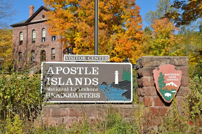 Apostle Islands National Lakeshore sign, with a large sandstone building in the back ground.
