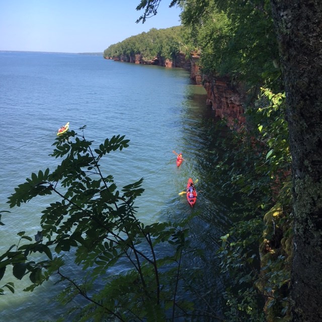 looking down from the trail on a sea kayak tour with an outfitter paddling along the caves