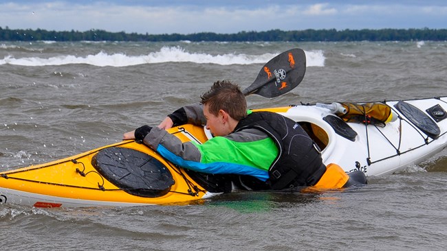 Person re-entering a tipped kayak in lake.