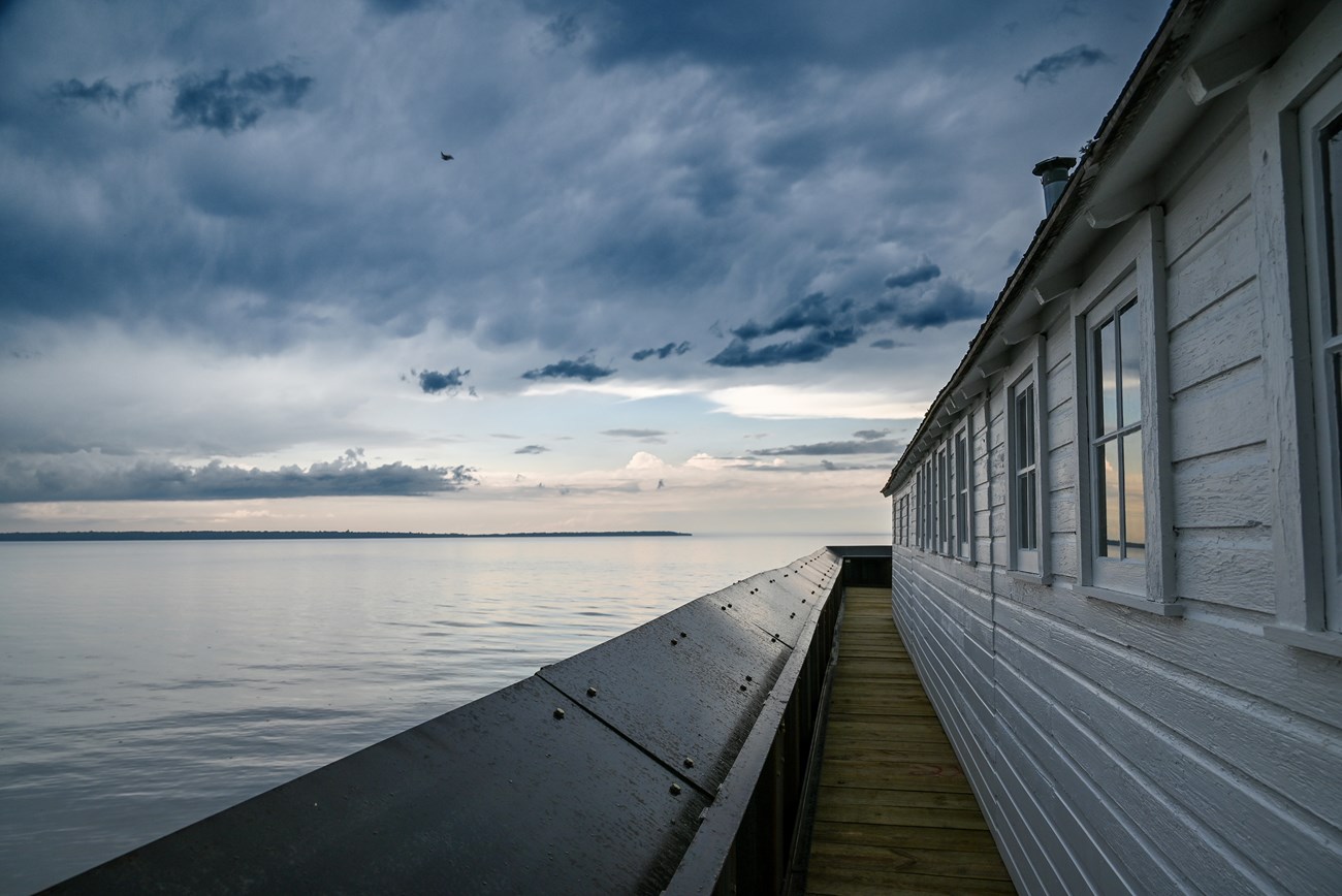 Photograph of boathouse and dock along lake with storm clouds approaching.