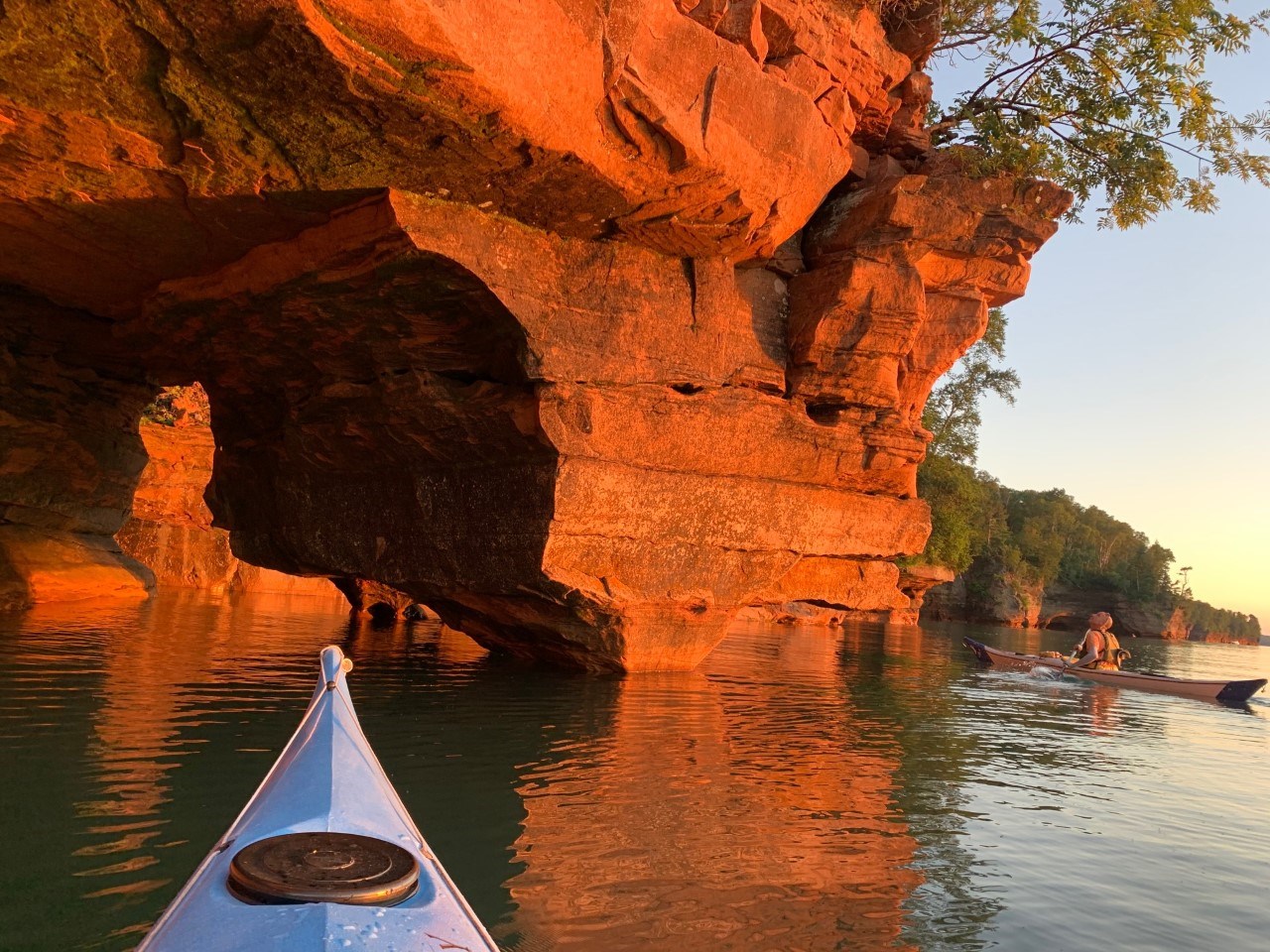 Two kayakers on the lake looking at a sandstone arch.