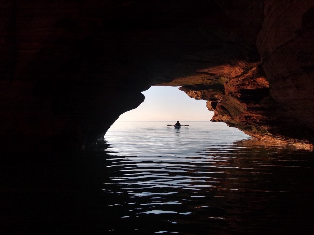 The Silhouette of a kayak under a rock arch on the water.