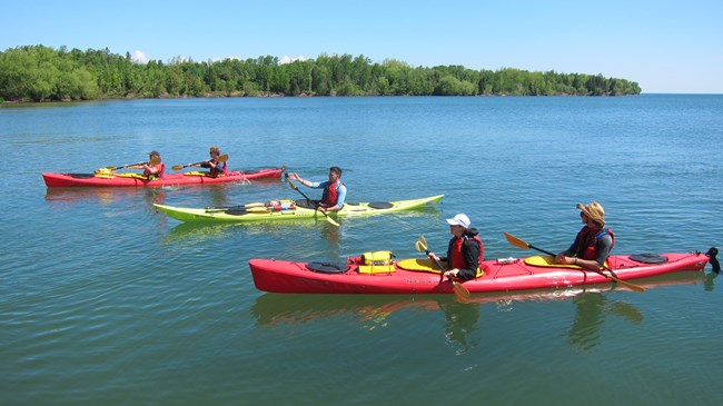 Two tandem kayaks and one single paddling on a calm lake.