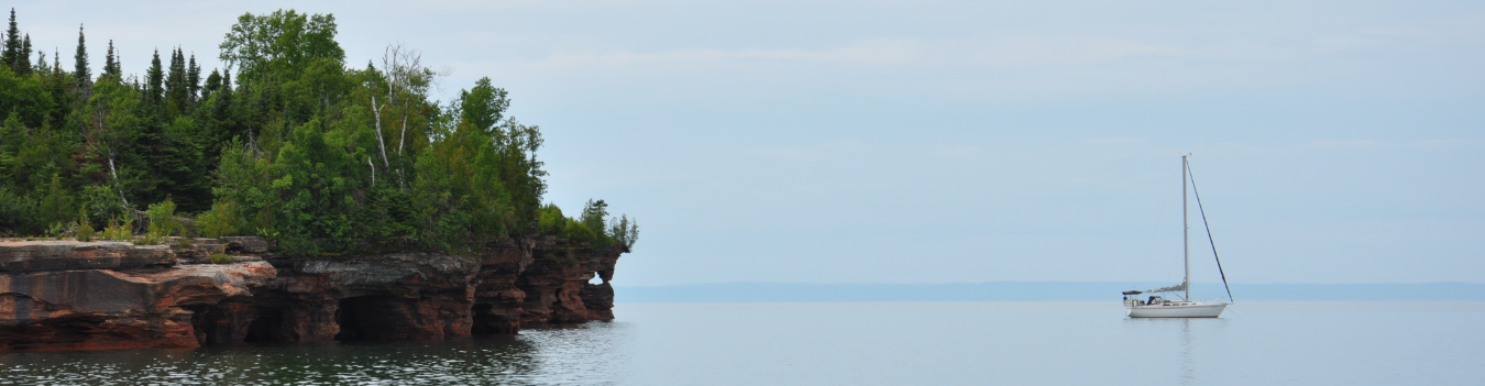 A sailboat on a lake next to a rocky shore with trees.