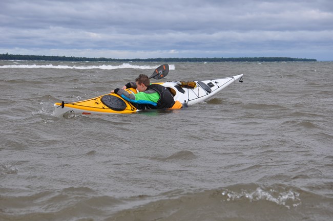 Person re-entering a tipped kayak in lake.