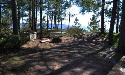 Tent pad shaded by white pine trees, with bear locker and picnic table in the background, overlooking Lake Superior.