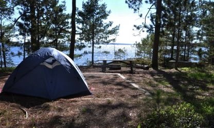Blue tent on the tent pad in the foreground, with picnic table, fire ring, and bear box, overlooking Lake Superior.