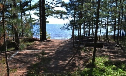 Tent pad, bear box, fire ring in campsite, overlooking Lake Superior on a sunny day.