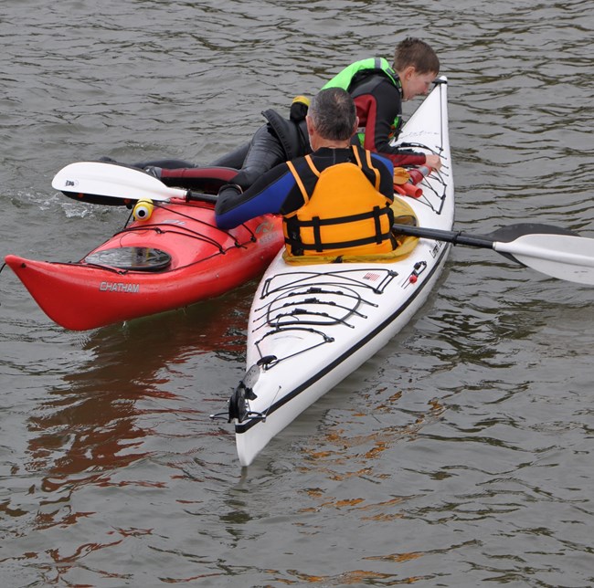 One person in a kayaking helping another capsized person re-enter their kayak on a lake.