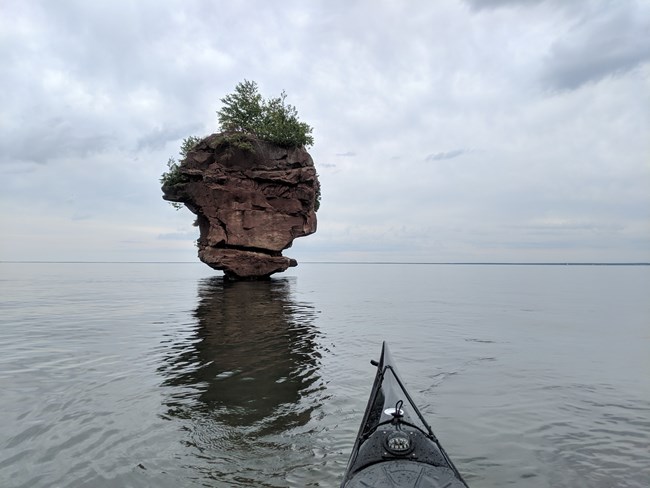 Large rock with vegetation growing on it surrounded by water.