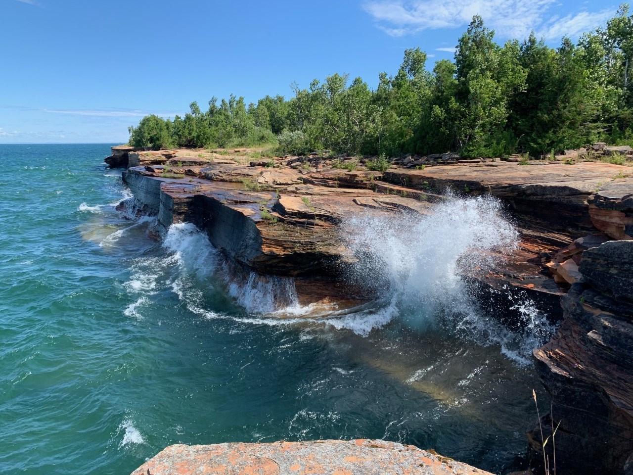 Big waves hit the sandstone cliffs creating sea spray.