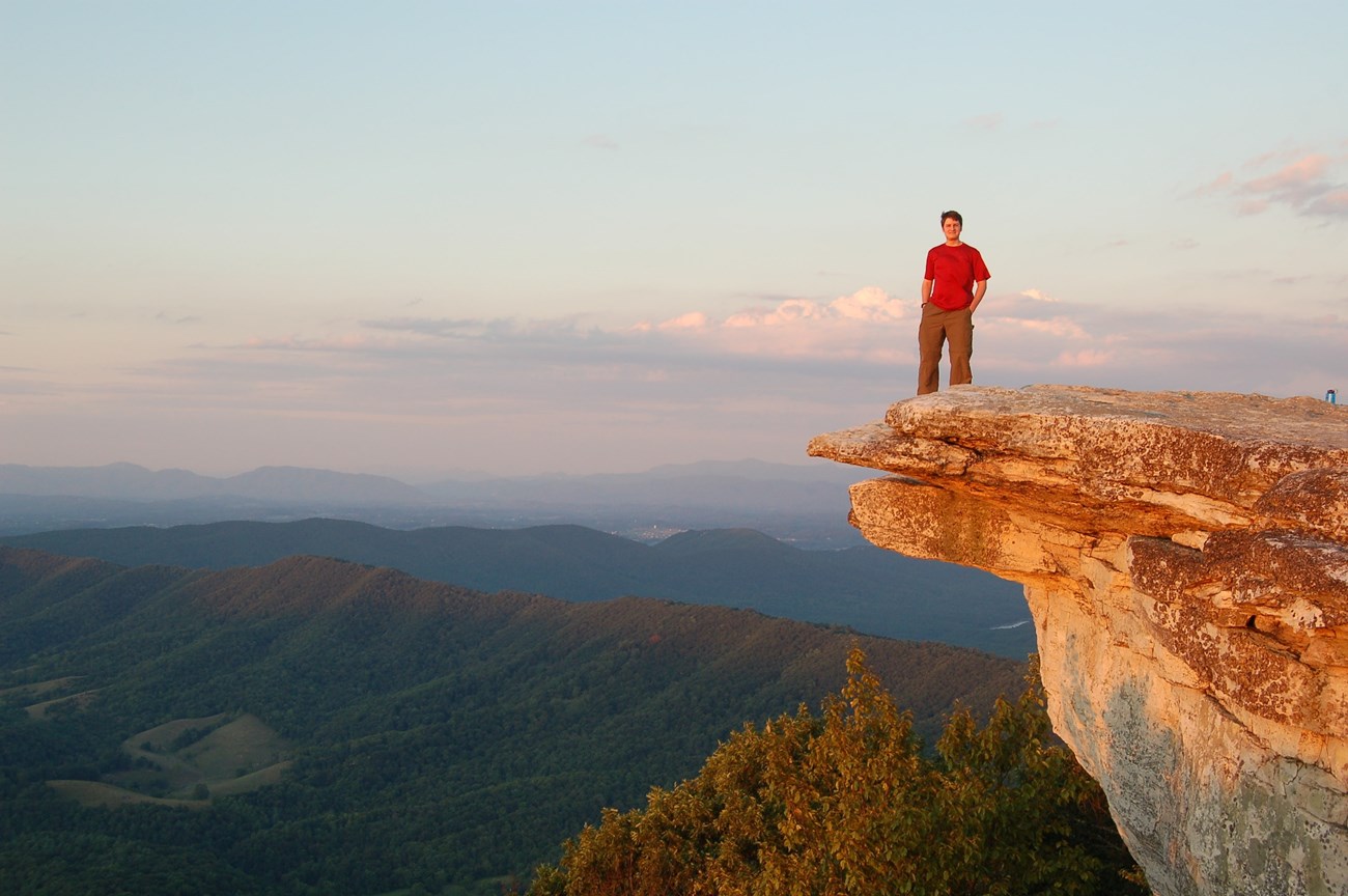 Man stands on McAfee Knob overlooking mountains.