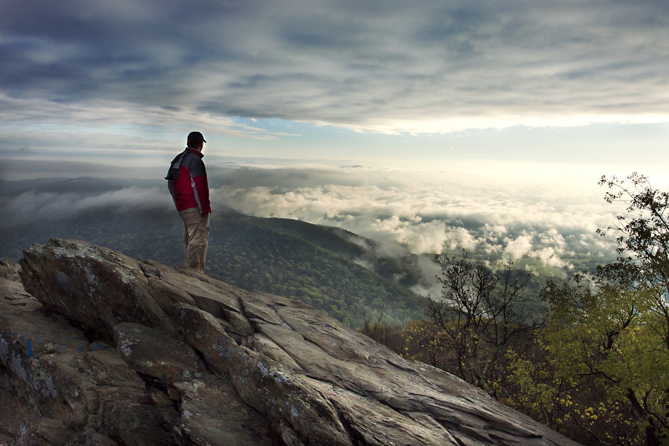 A man stands on rocks overlooking the mountains in the distance