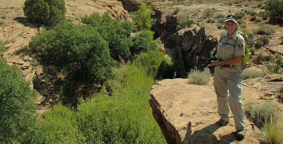 a woman in volunteer uniform stands at the edge of a small canyon