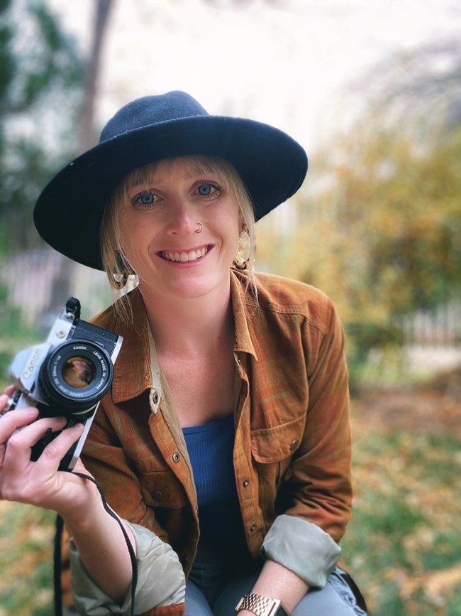 blond woman in black hat with DSLR camera