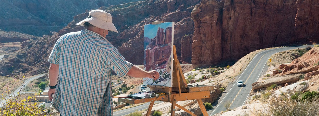 an artist paints on an easel overlooking a road