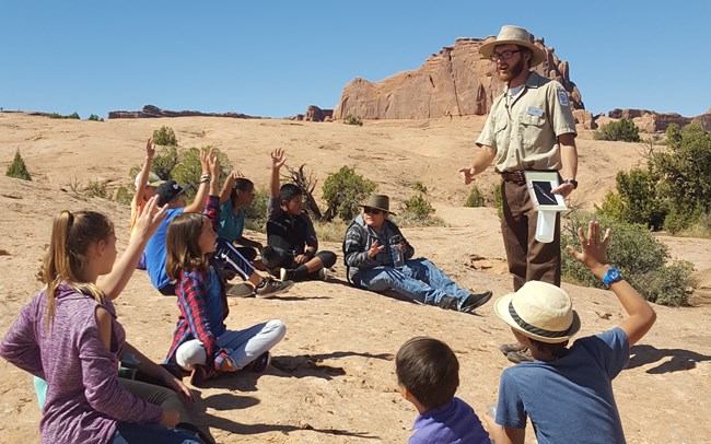 Park volunteer addresses school group seated on slickrock