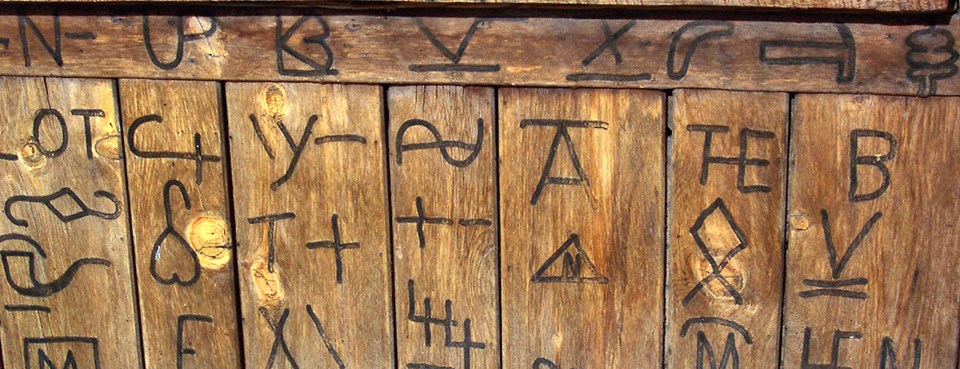 Wood planks with cattle brands burned into them. The brands consist of letter, numbers, and symbols.