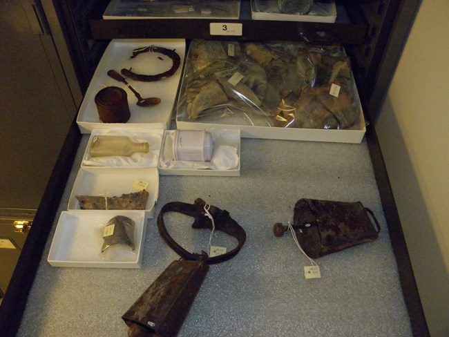 Museum Cabinet Photograph of contents in a museum cabinet. A historic cow bell and sheep bell, glass containers, a horseshoe, a fork and a tin can.